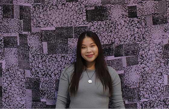 woman with long brown hair standing in front of purple printed background